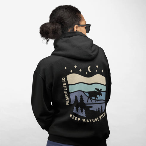 This hoodie features a moose silhouette roaming across prairie hills, pine trees with stars scattered above and a crescent moon glowing softly.