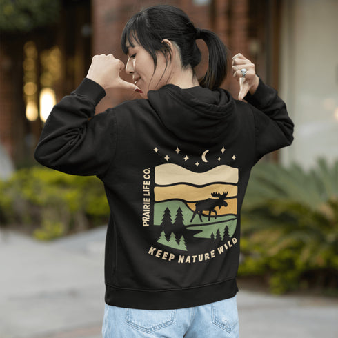 This premium hoodie features a moose silhouette wandering across prairie hills, Pine trees and a clear night sky filled with stars and a crescent moon.