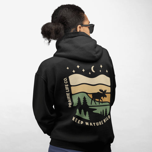 This premium hoodie features a moose silhouette wandering across prairie hills, Pine trees and a clear night sky filled with stars and a crescent moon.