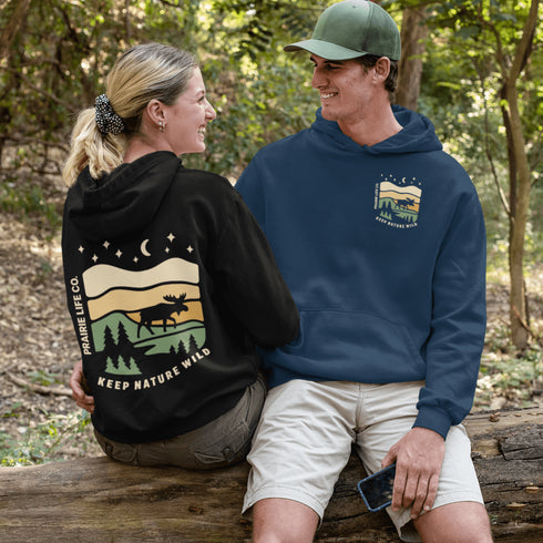 This premium hoodie features a moose silhouette wandering across prairie hills, Pine trees and a clear night sky filled with stars and a crescent moon.