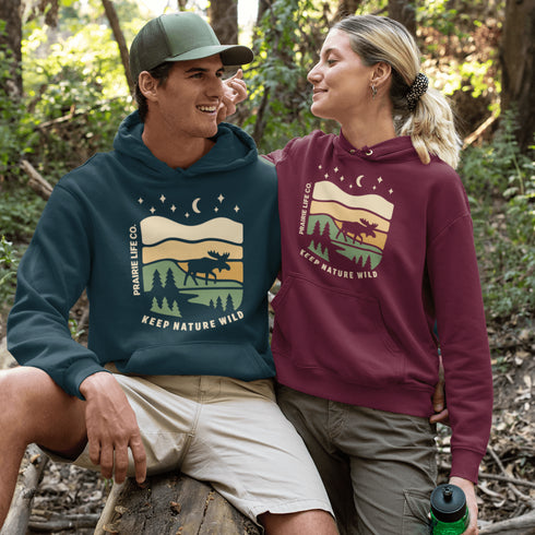 Featuring a bold moose silhouette layered over rolling hills, pine trees, and a starry night sky, this hoodie is a tribute to Canada’s wild landscapes.