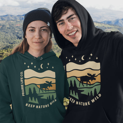 Featuring a bold moose silhouette layered over rolling hills, pine trees, and a starry night sky, this hoodie is a tribute to Canada’s wild landscapes.
