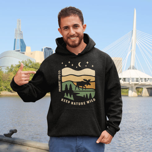 Featuring a bold moose silhouette layered over rolling hills, pine trees, and a starry night sky, this hoodie is a tribute to Canada’s wild landscapes.