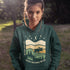 Featuring a bold moose silhouette layered over rolling hills, pine trees, and a starry night sky, this hoodie is a tribute to Canada’s wild landscapes.