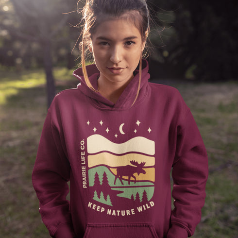 Featuring a bold moose silhouette layered over rolling hills, pine trees, and a starry night sky, this hoodie is a tribute to Canada’s wild landscapes.