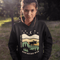 Featuring a bold moose silhouette layered over rolling hills, pine trees, and a starry night sky, this hoodie is a tribute to Canada’s wild landscapes.