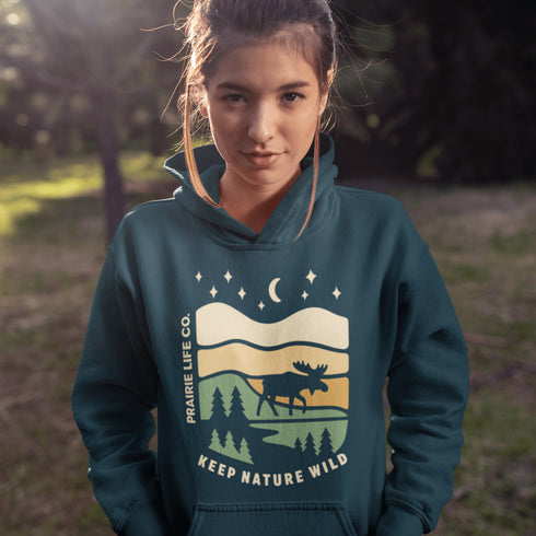 Featuring a bold moose silhouette layered over rolling hills, pine trees, and a starry night sky, this hoodie is a tribute to Canada’s wild landscapes.