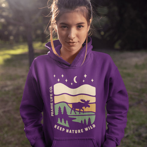 Featuring a bold moose silhouette layered over rolling hills, pine trees, and a starry night sky, this hoodie is a tribute to Canada’s wild landscapes.