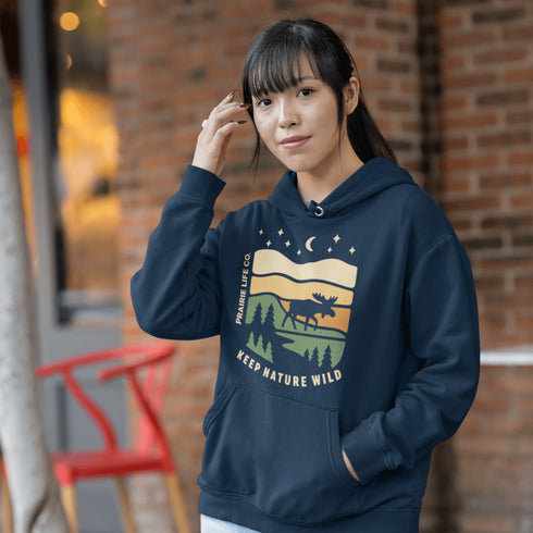 Featuring a bold moose silhouette layered over rolling hills, pine trees, and a starry night sky, this hoodie is a tribute to Canada’s wild landscapes.