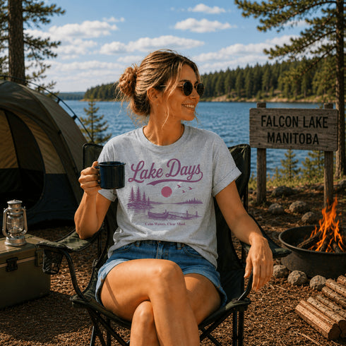 Woman sitting by a campfire at Falcon Lake, Manitoba, holding a mug with 'Lake Days' t-shirt on.