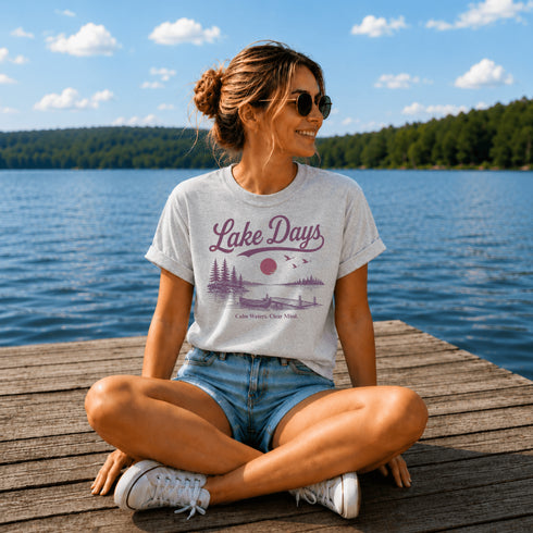 Woman sitting on a dock by a lake wearing a 'Lake Days' t-shirt.