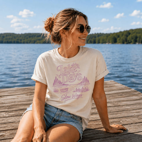 Woman sitting on a dock by a lake wearing a t-shirt with a graphic design.