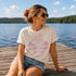 Woman sitting on a dock by a lake wearing a t-shirt with a graphic design.