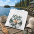 White t-shirt with 'Lake Life' design on a wooden dock by a lake with a cabin in the background.
