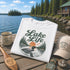 White t-shirt with 'Lake Life' design on a wooden dock by a lake with a cabin in the background.
