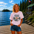 Woman wearing a vintage Lake Life loon graphic t-shirt while standing on a dock overlooking Falcon Lake, Manitoba with pine trees, a lakeside cabin, and a peaceful Canadian lake in the background.