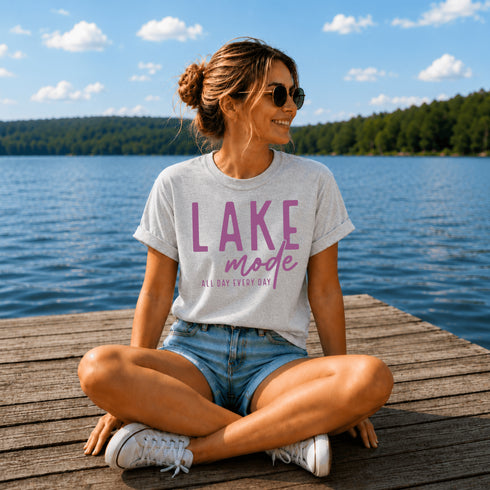 Woman sitting on a dock by a lake wearing a 'Lake Mode' t-shirt.