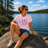 Woman sitting by a lake wearing a pink 'Lake Mode' t-shirt.