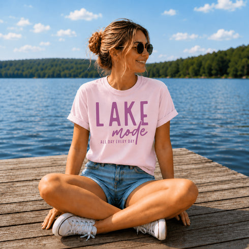 Woman sitting on a dock by a lake wearing a 'Lake Mode' t-shirt.
