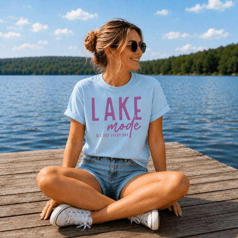 Woman sitting on a dock by a lake wearing a 'Lake Mode' t-shirt.