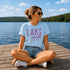 Woman sitting on a dock by a lake wearing a 'Lake Mode' t-shirt.