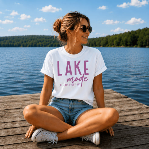 Woman sitting on a dock by a lake wearing a 'Lake Mode' t-shirt.