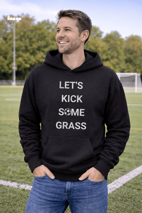 Man wearing a black hoodie with 'LET'S KICK SOME GRASS' text on a soccer field.