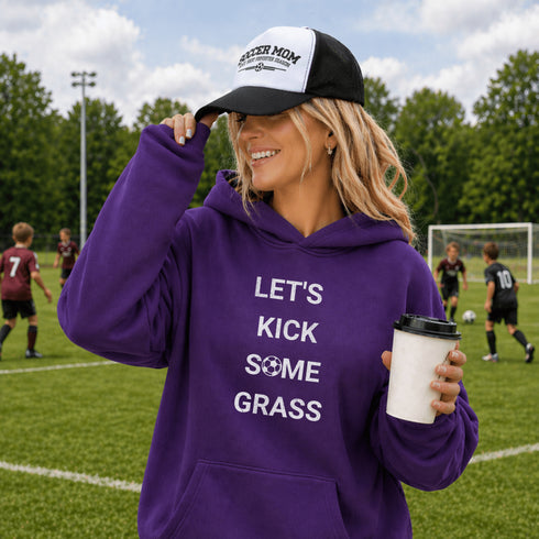 Woman on a soccer field wearing a purple hoodie with text and a black and white cap.