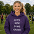 Woman wearing a purple hoodie with 'Let's Kick Some Grass' text on a soccer field.