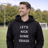 Man wearing a black hoodie with 'LET'S KICK SOME GRASS' text on a sports field.