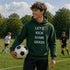 Person wearing a green hoodie with text holding a soccer ball on a sports field.