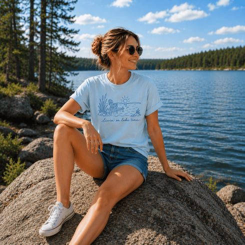 Woman sitting on a rock by a lake wearing a t-shirt with a graphic design.