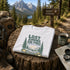 Folded t-shirt with nature-themed design on a wooden stump in a forest setting with a 'Banff Canada' sign.