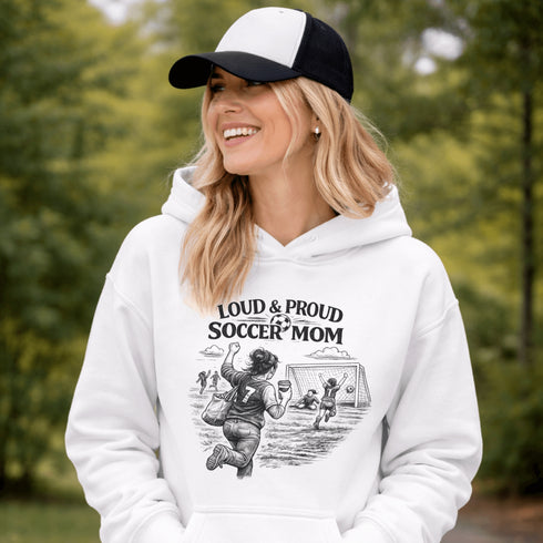 Woman wearing a grey Loud & Proud Soccer Mom hoodie with a vintage soccer scene design, standing on a soccer field with hands in pocket
