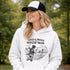 Woman wearing a grey Loud & Proud Soccer Mom hoodie with a vintage soccer scene design, standing on a soccer field with hands in pocket