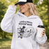 Woman wearing a grey Loud & Proud Soccer Mom hoodie with a vintage soccer scene design, standing on a soccer field with hands in pocket