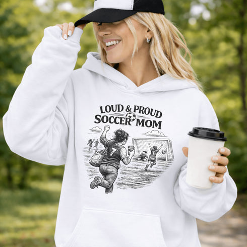 Woman wearing a white Loud & Proud Soccer Mom hoodie with a vintage soccer scene design, standing on a soccer field with hands in pocket