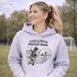 Woman wearing a grey Loud & Proud Soccer Mom hoodie with a vintage soccer scene design, standing on a soccer field with hands in pocket
