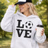 Hoodie with bold LOVE design featuring a soccer ball replacing the O, worn by woman holding coffee cup outdoors