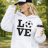 Hoodie with bold LOVE design featuring a soccer ball replacing the O, worn by woman holding coffee cup outdoors