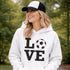 Hoodie with bold LOVE design featuring a soccer ball replacing the O, worn by woman holding coffee cup outdoors