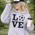 Hoodie with bold LOVE design featuring a soccer ball replacing the O, worn by woman holding coffee cup outdoors