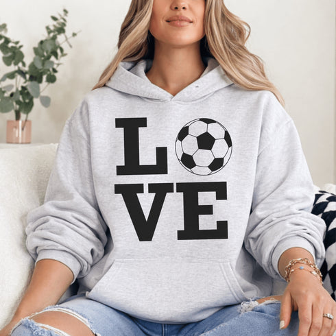 Hoodie with bold LOVE design featuring a soccer ball replacing the O, worn by woman holding coffee cup outdoors