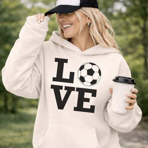 Hoodie with bold LOVE design featuring a soccer ball replacing the O, worn by woman holding coffee cup outdoors