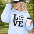Hoodie with bold LOVE design featuring a soccer ball replacing the O, worn by woman holding coffee cup outdoors