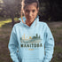person wearing manitoba prairie life hoodie with farm and wheat field design standing in prairie field