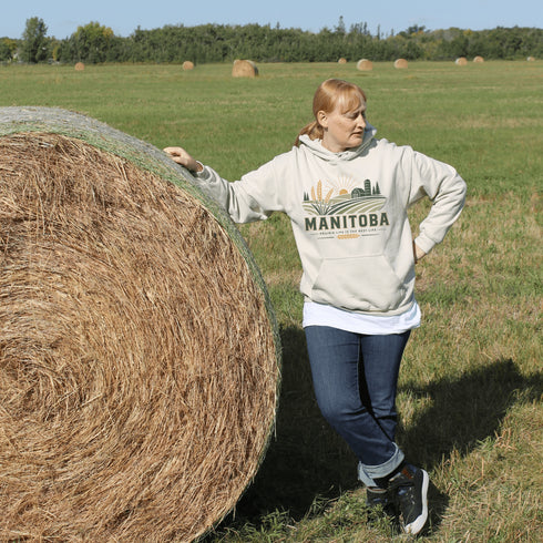 person wearing manitoba prairie life hoodie with farm and wheat field design standing in prairie field