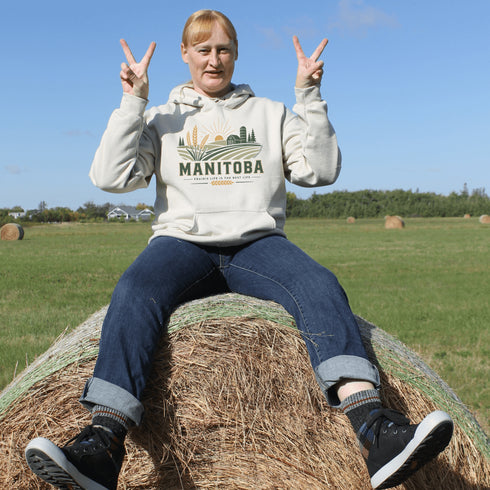 person wearing manitoba prairie life hoodie with farm and wheat field design standing in prairie field