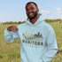 person wearing manitoba prairie life hoodie with farm and wheat field design standing in prairie field