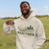 person wearing manitoba prairie life hoodie with farm and wheat field design standing in prairie field